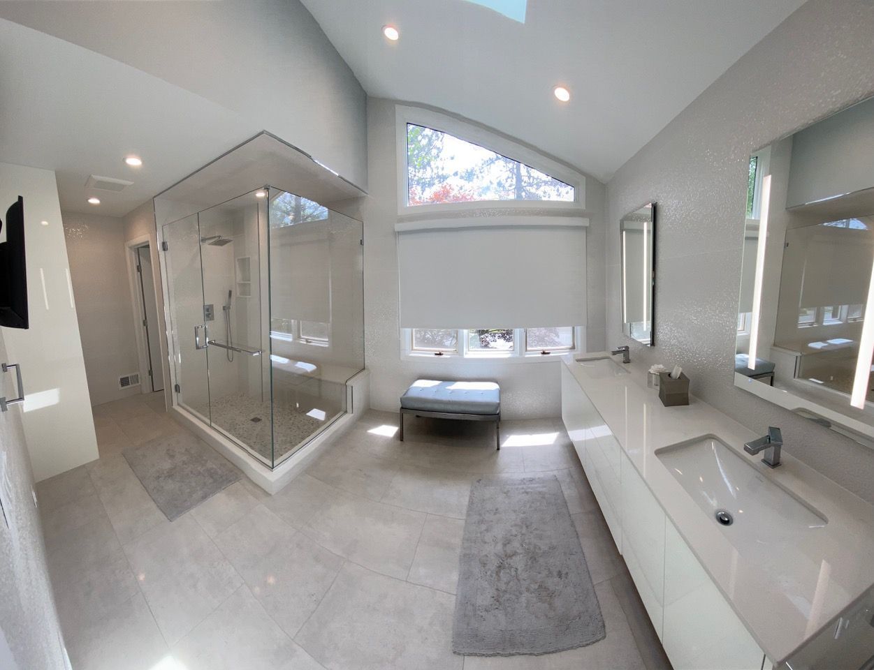 Modern white bathroom with large shower, double sinks, and a large window.