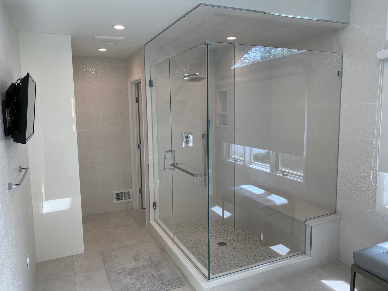 Bathroom with a tub, shower, and window. Neutral-toned tile and a clear glass shower door.
