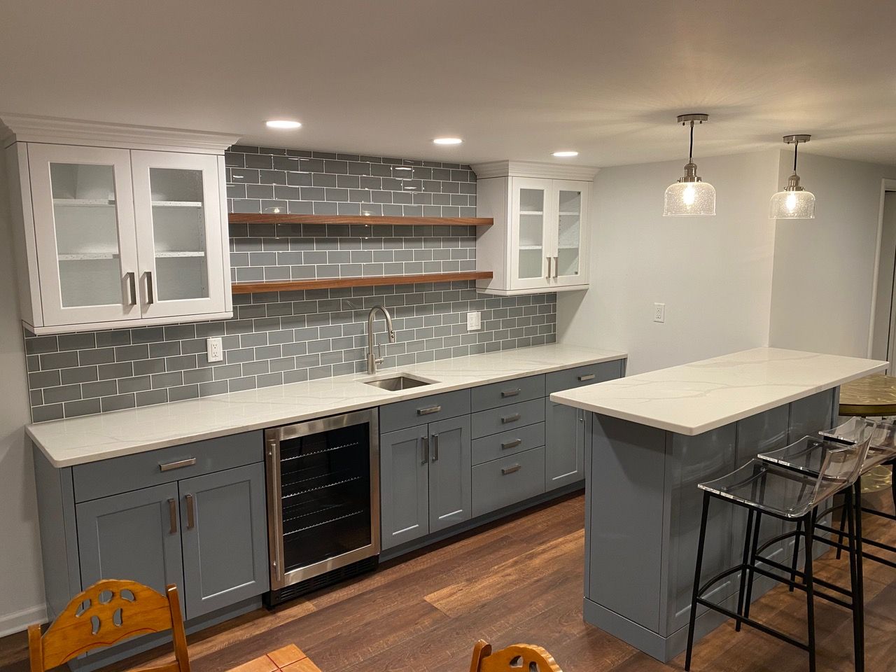 Modern basement bar with gray cabinets, white countertops, and subway tile backsplash.