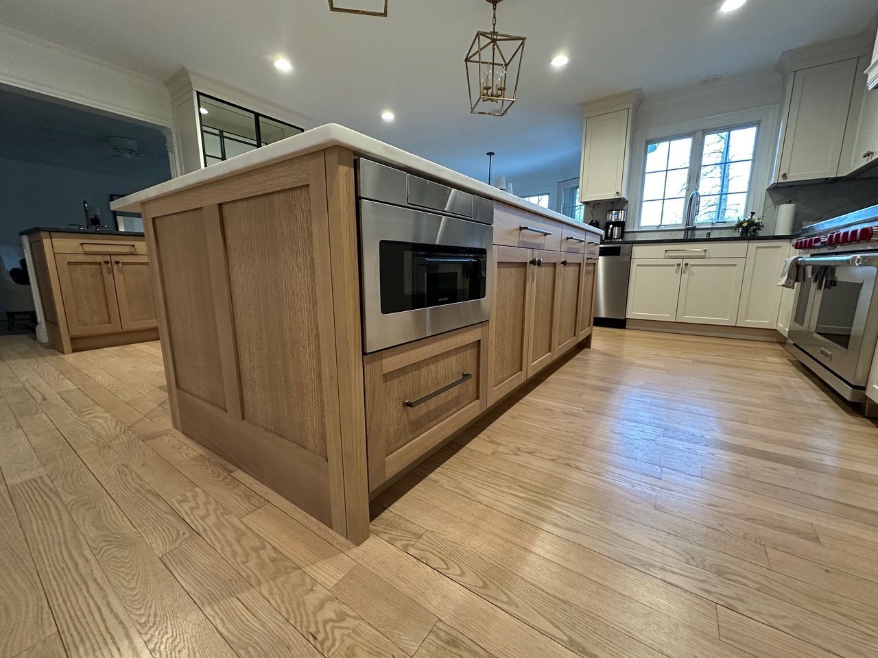 Kitchen island with light wood cabinets, stainless steel microwave, and white countertop. Light wood floor.