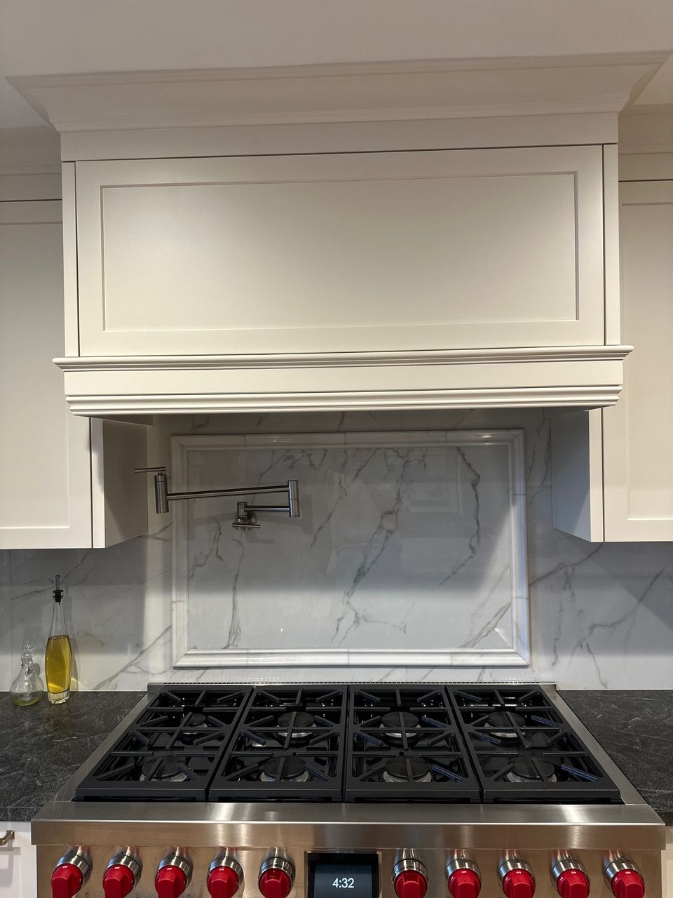 White kitchen range hood above a gas stove with marble backsplash.