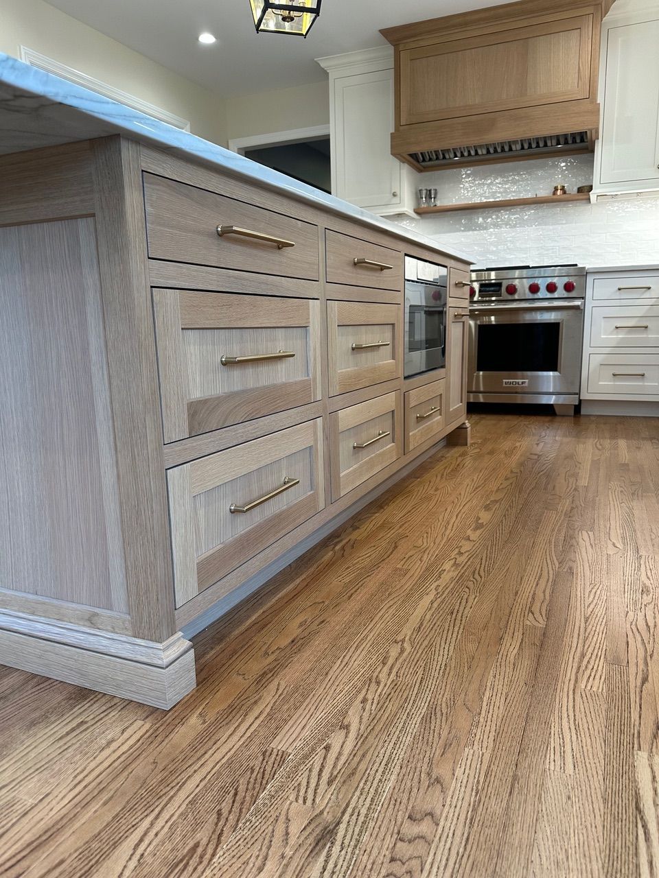 Kitchen island with light wood cabinets and gold hardware, hardwood floors.