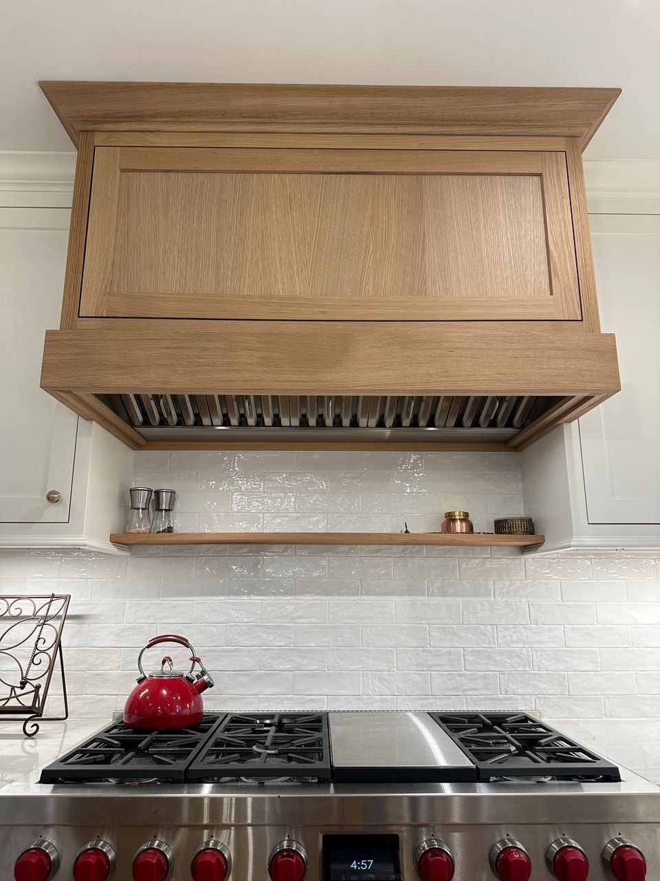 Wooden range hood above a stainless steel stove with a red teapot.