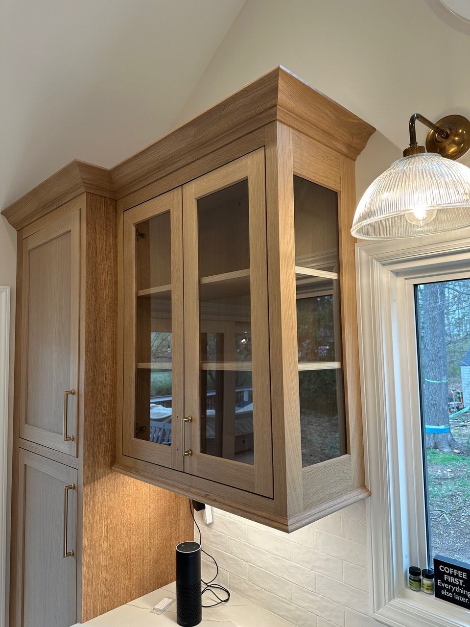 Light wood kitchen cabinets with glass doors, above a countertop and near a window.