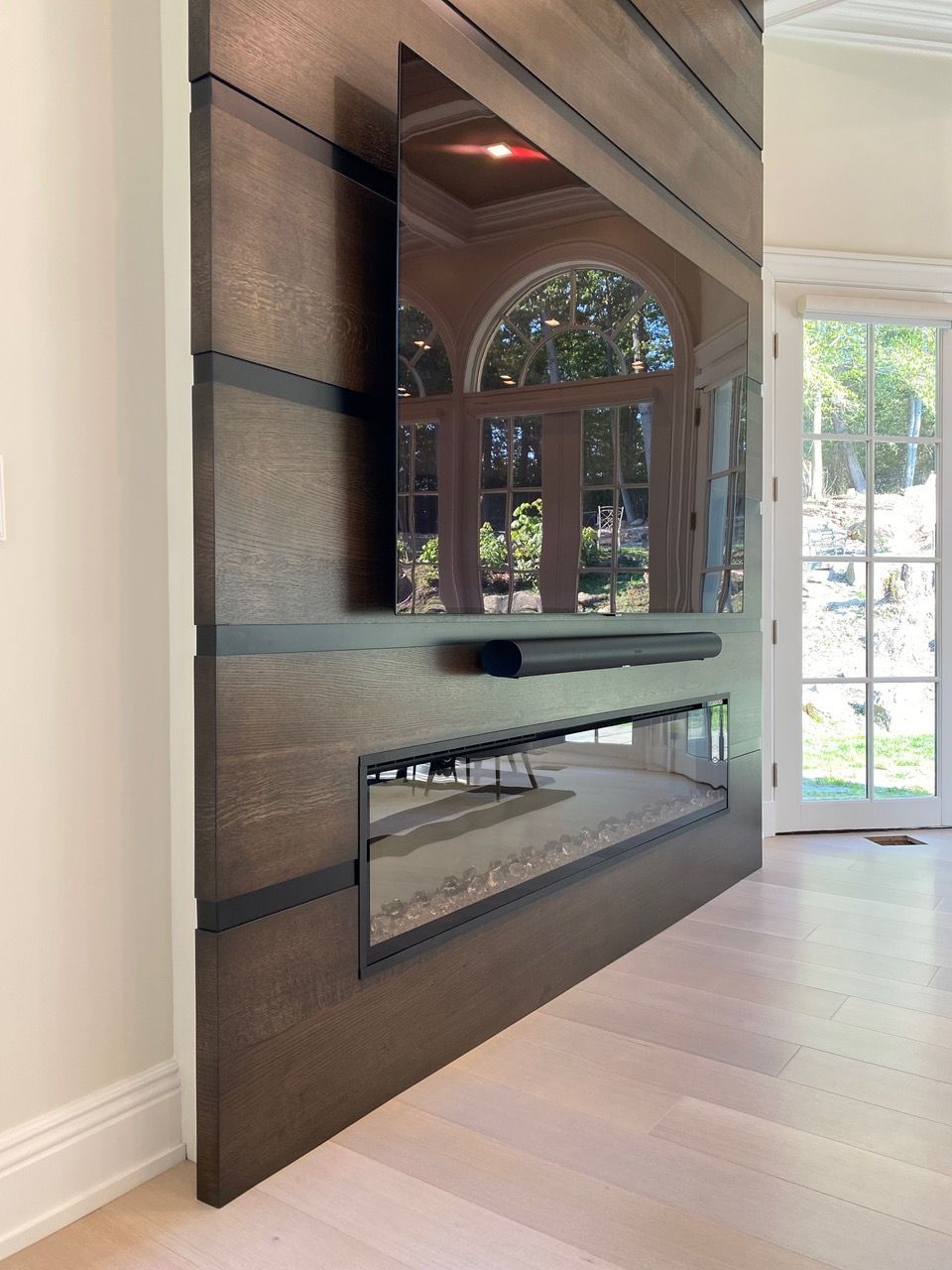 Wooden panel wall with built-in fireplace and TV; a large window is reflected on the screen.