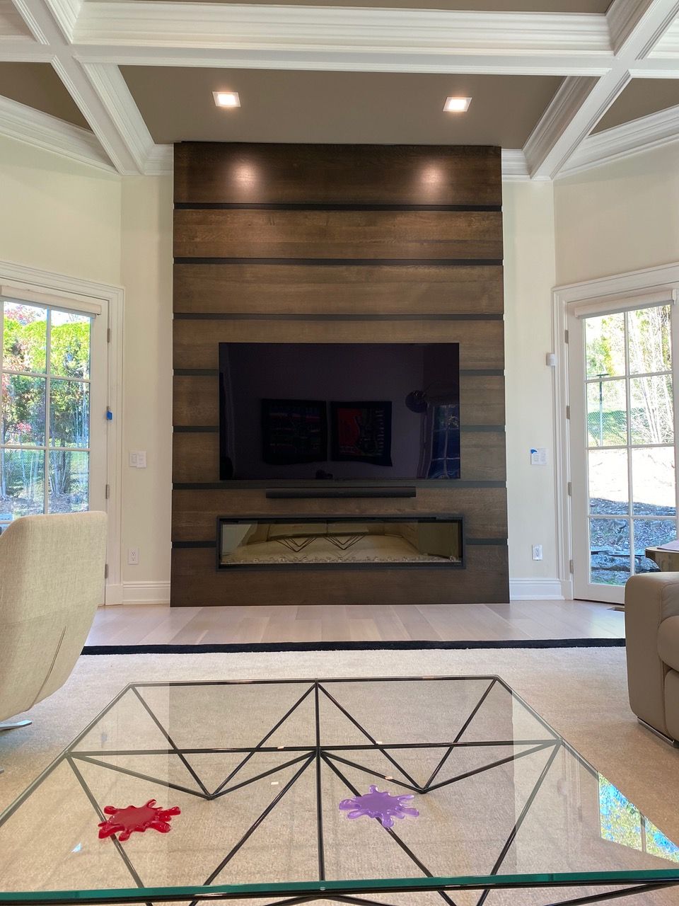 Living room with large TV, fireplace, and glass coffee table. Wooden accent wall with recessed lighting.
