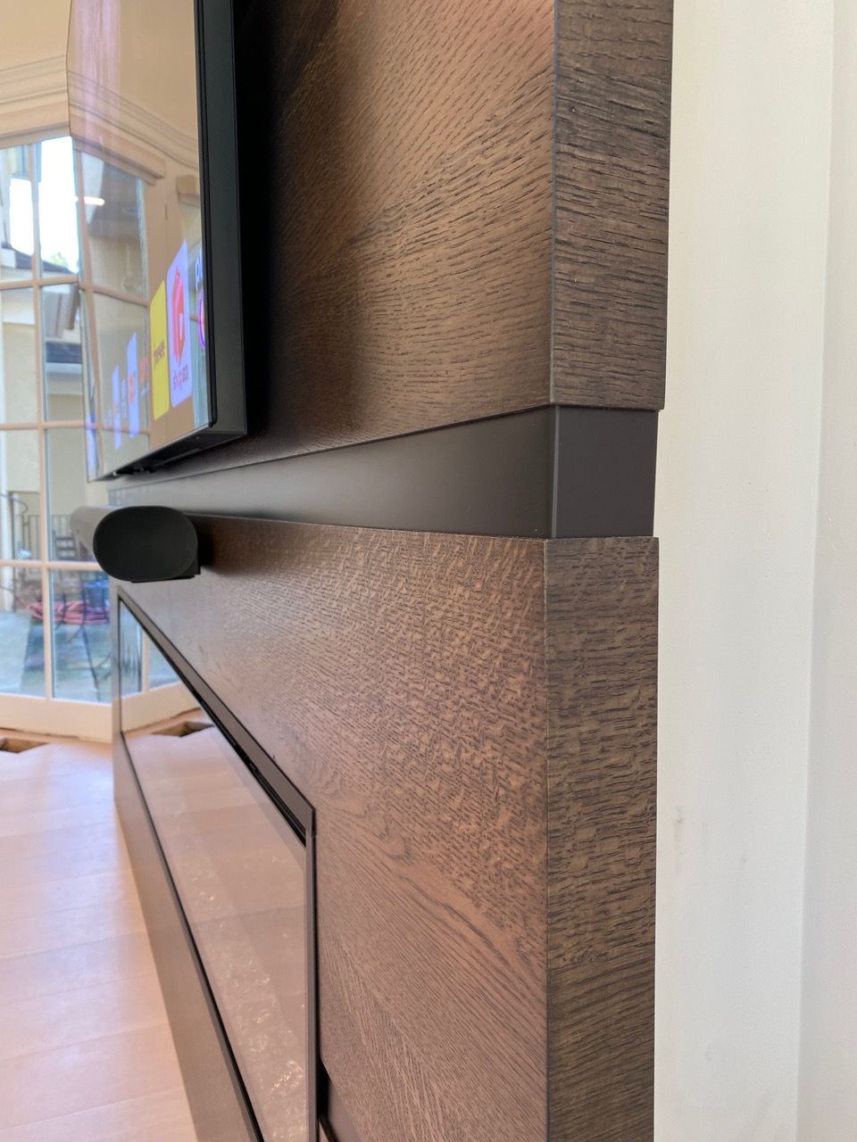 Close-up of a wood-paneled fireplace surround with a mounted TV, speaker, and black trim.