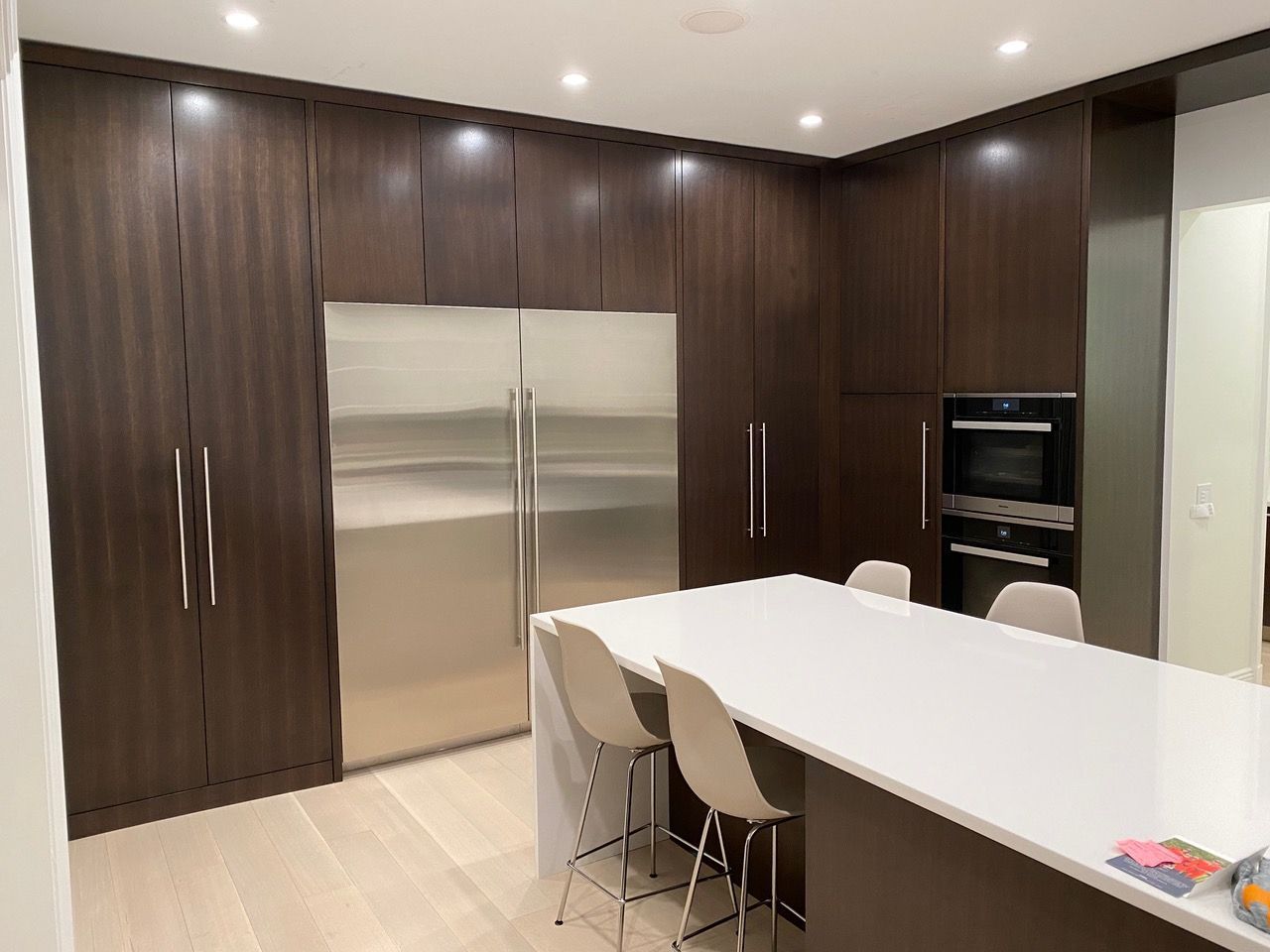 Modern kitchen with dark wood cabinets, stainless steel refrigerator, white island, and light wood floor.