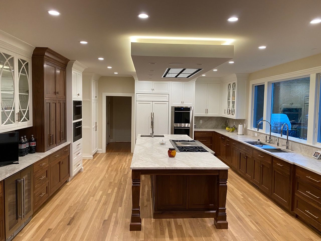 Spacious kitchen with wood floors, brown and white cabinets, island with cooktop, and recessed lighting.
