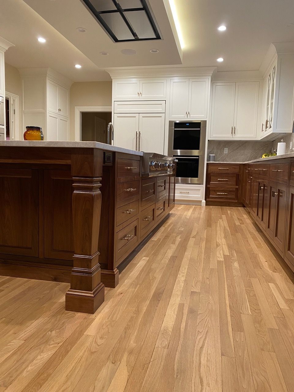 Spacious kitchen with wood floors and dark brown island. White cabinets, recessed lighting, and built-in appliances.
