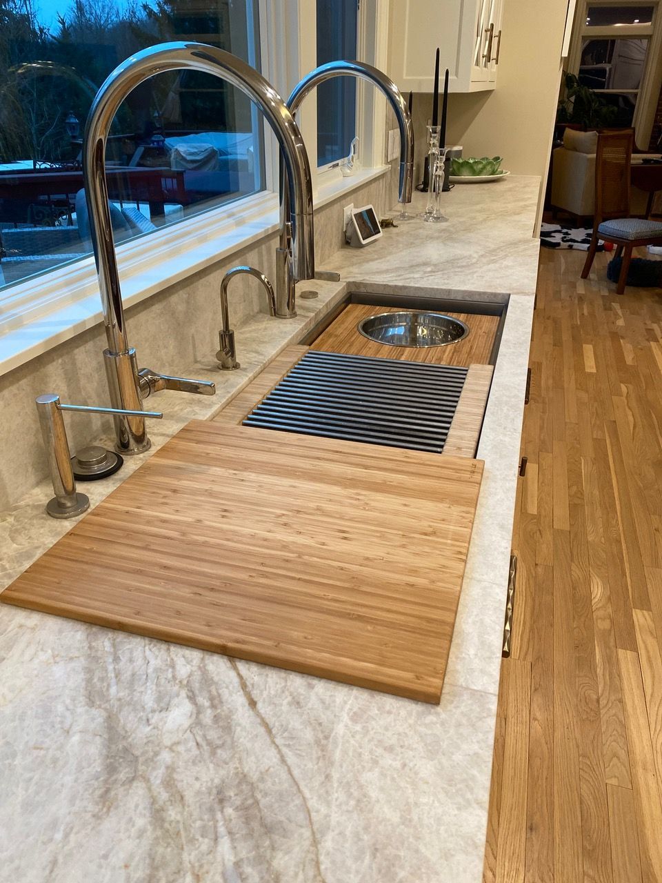 Kitchen sink with wooden cutting board and chrome faucet on a light-colored countertop.