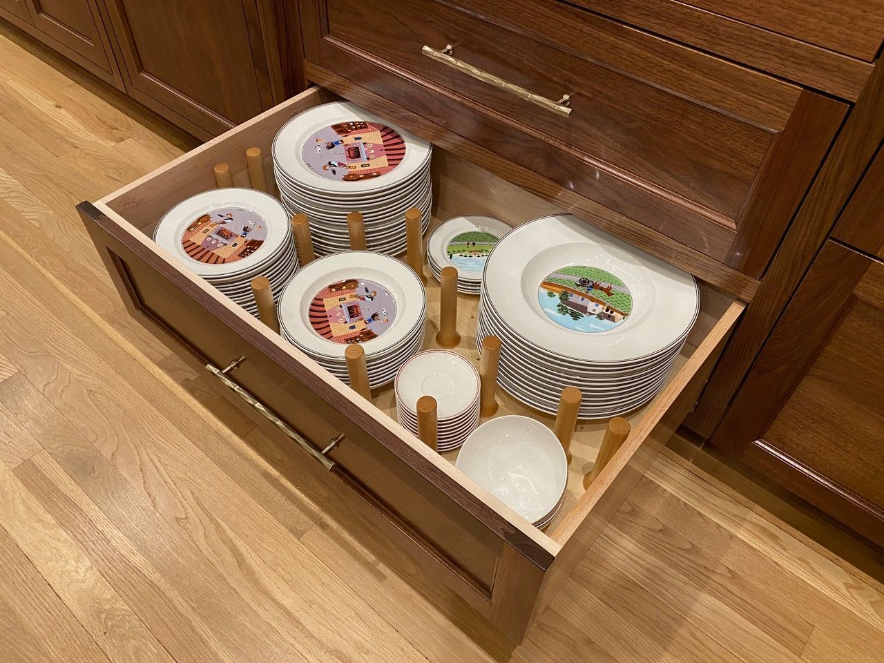 Wooden kitchen drawer with plates and bowls separated by wooden pegs.