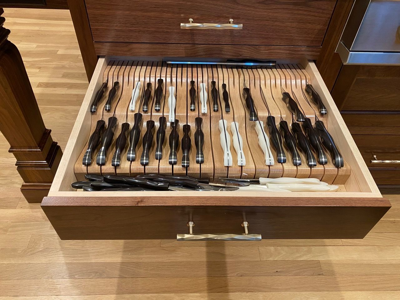 Wooden drawer open, revealing silverware neatly organized in slots.