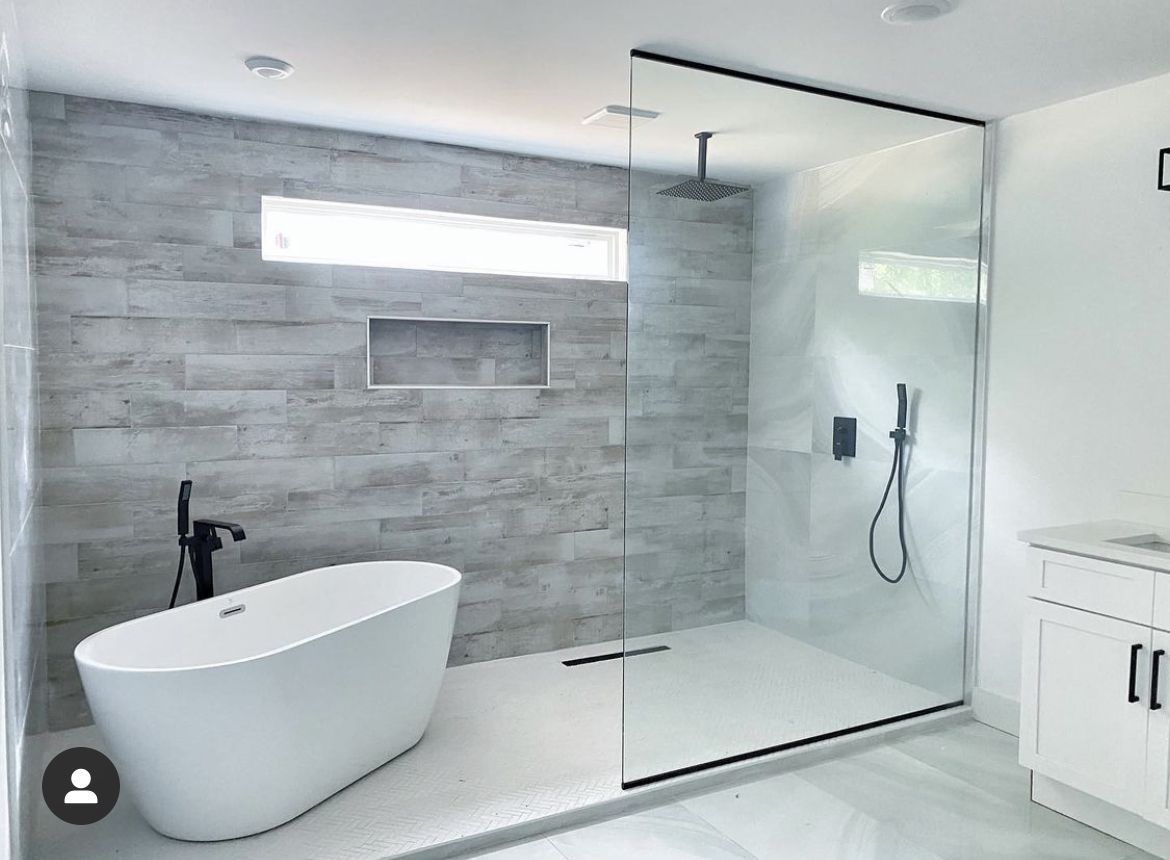 Modern bathroom with white tub, gray tiled accent wall, glass shower, and white vanity.