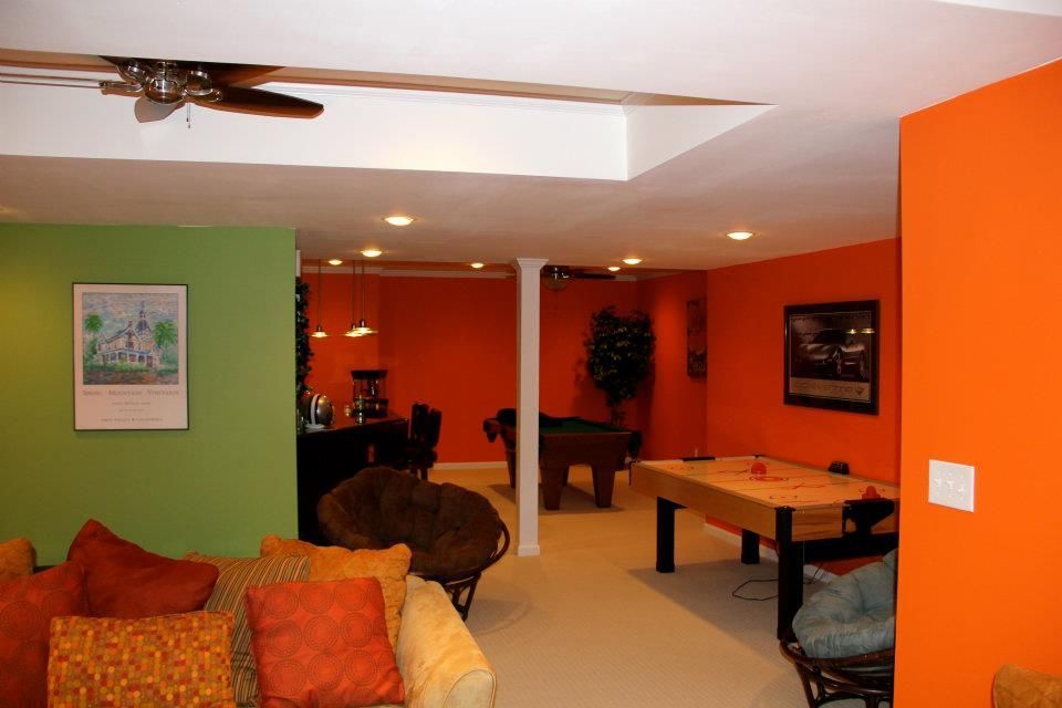 Living room with orange and green walls, featuring a pool table and seating.