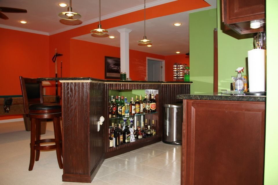 Home bar with dark wood, bottles, orange and green walls, and a stool.
