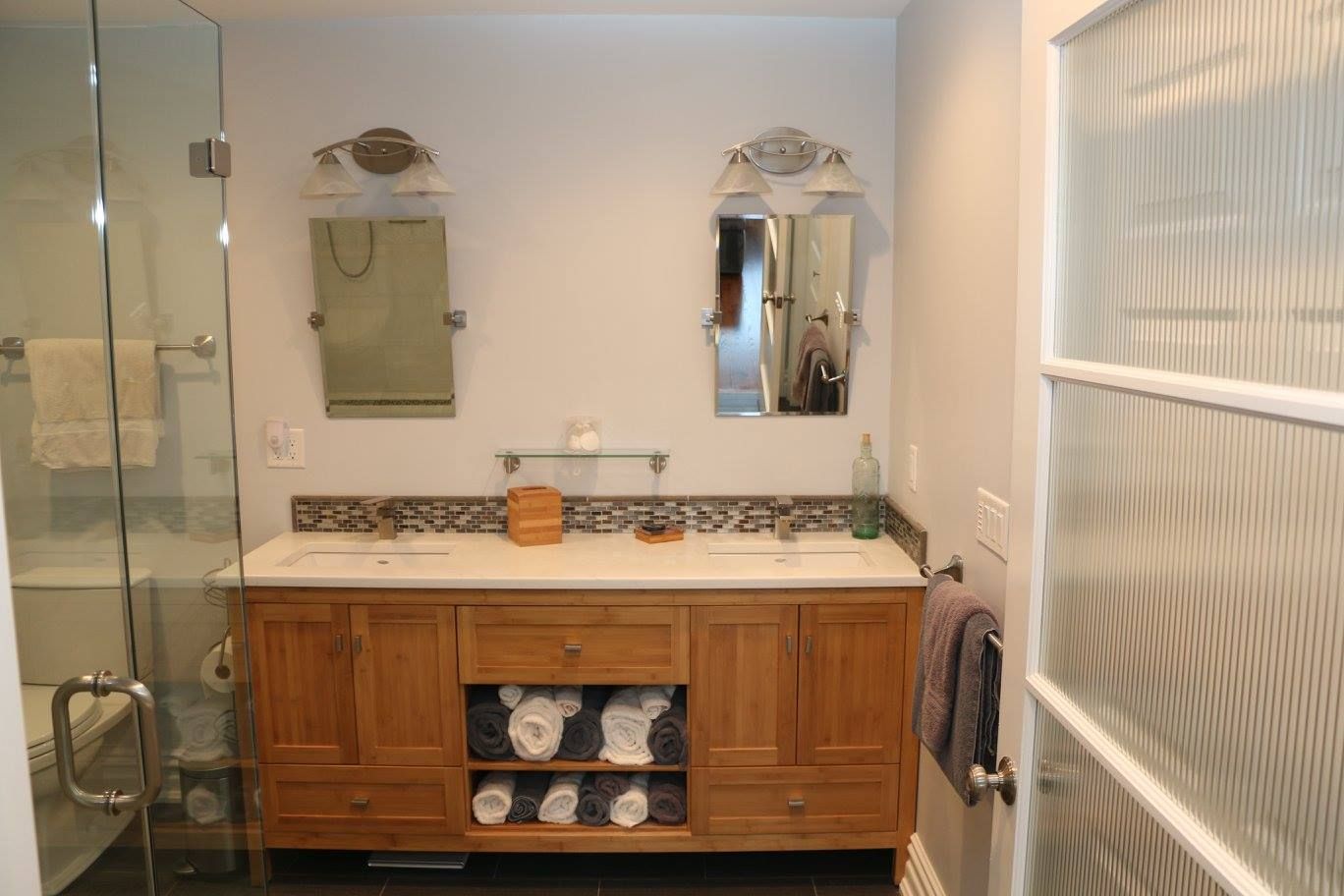 Bathroom with double vanity, two mirrors, glass shower, and frosted glass door.