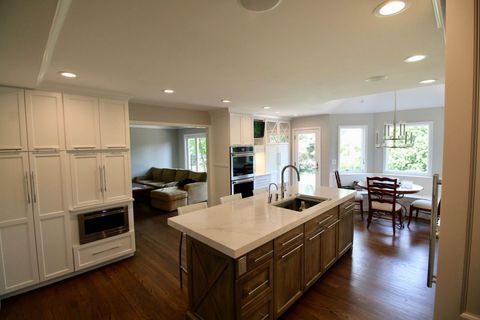 Open-concept kitchen with white and wood cabinets, island with sink, dining area, and living room beyond.