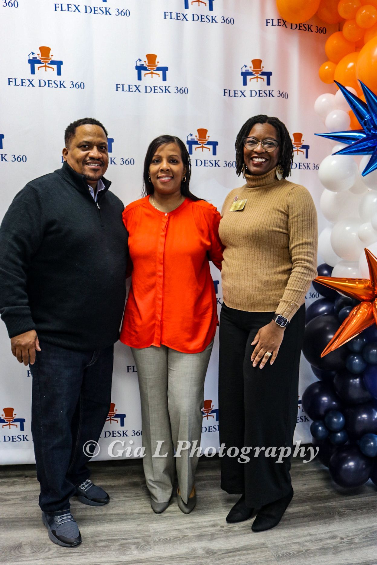 A man and two women are posing for a picture in front of balloons.