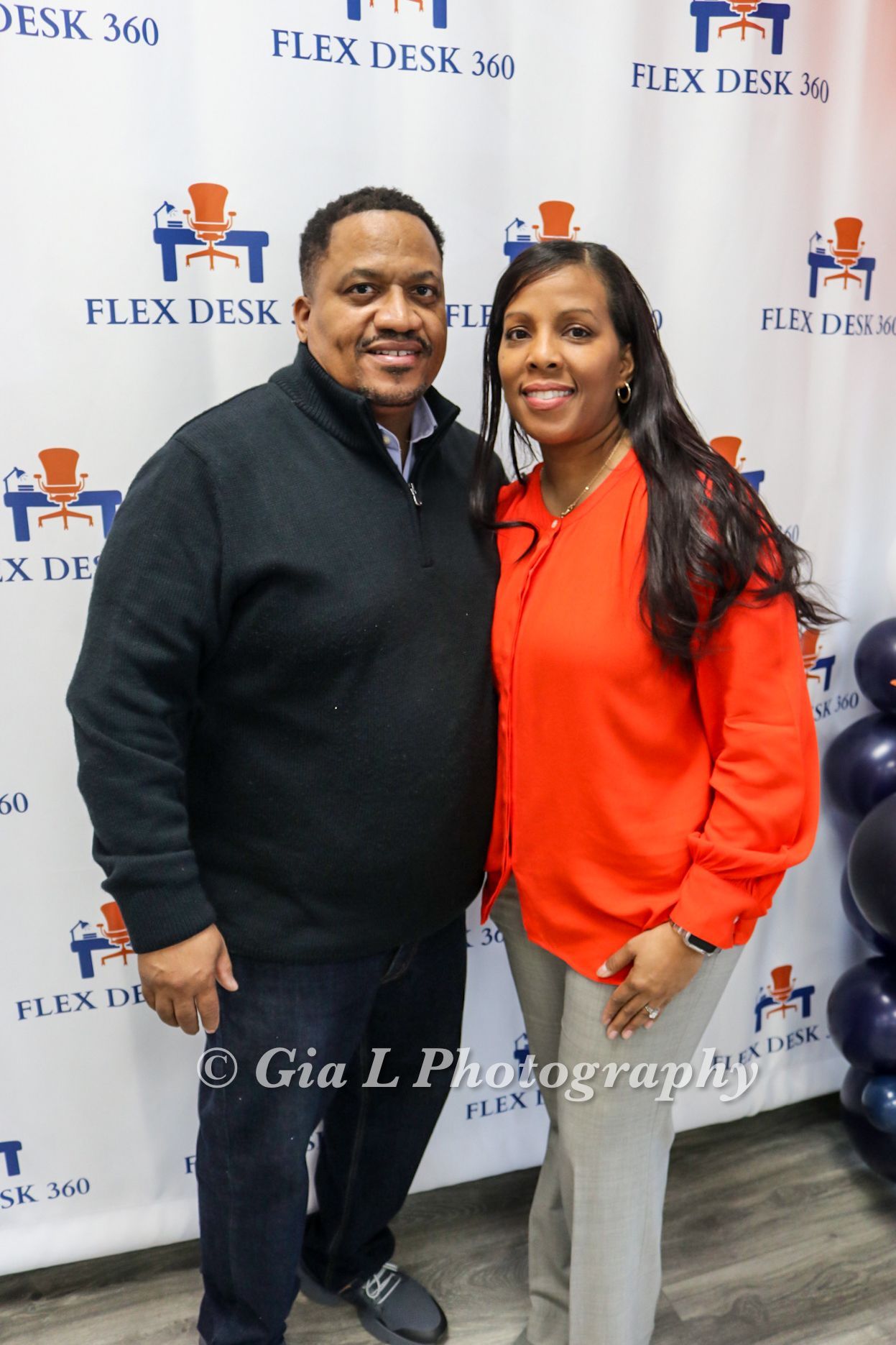 A man and a woman are posing for a picture in front of a flex desk 360 banner