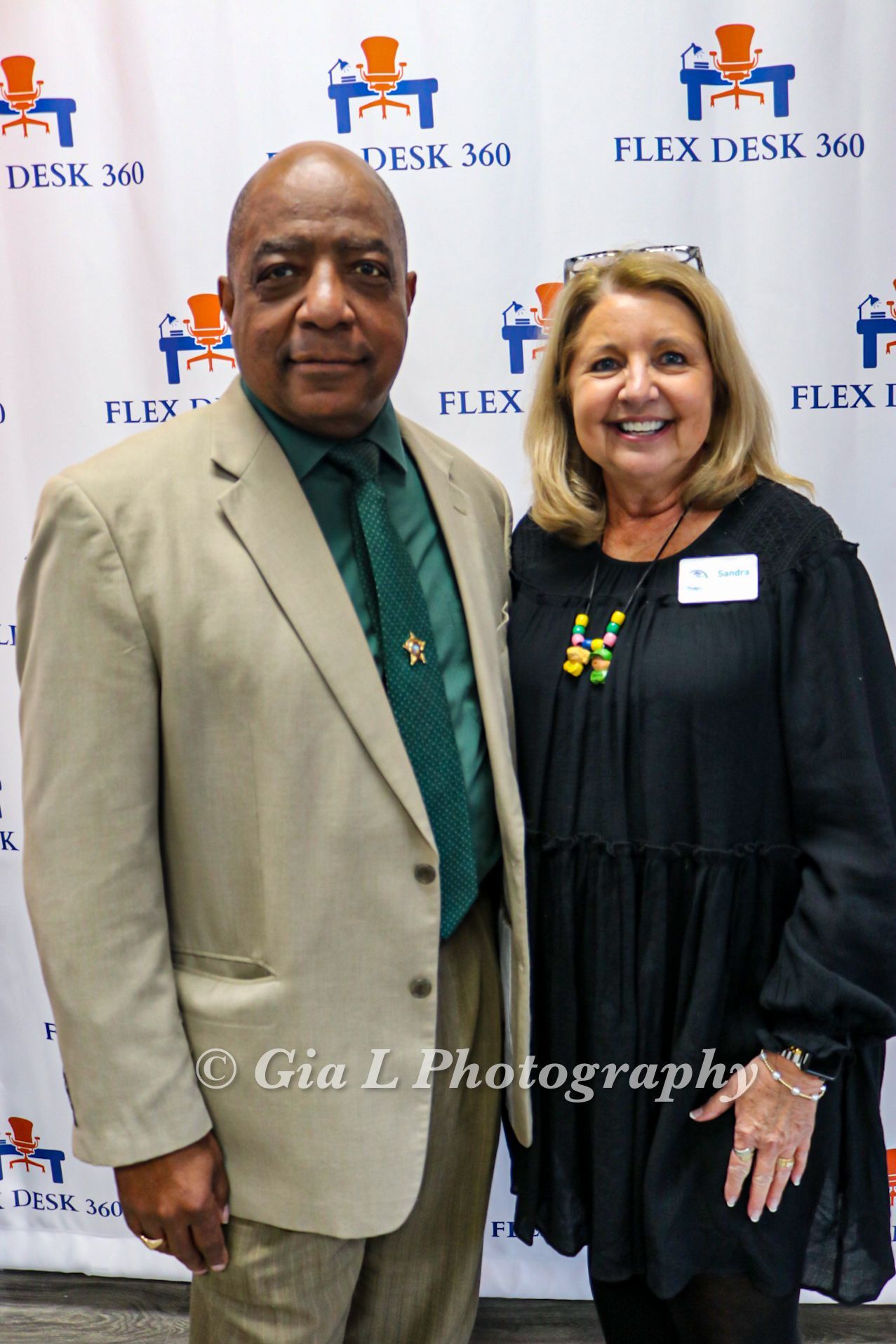 A man and a woman are posing for a picture in front of a flex desk 360 banner