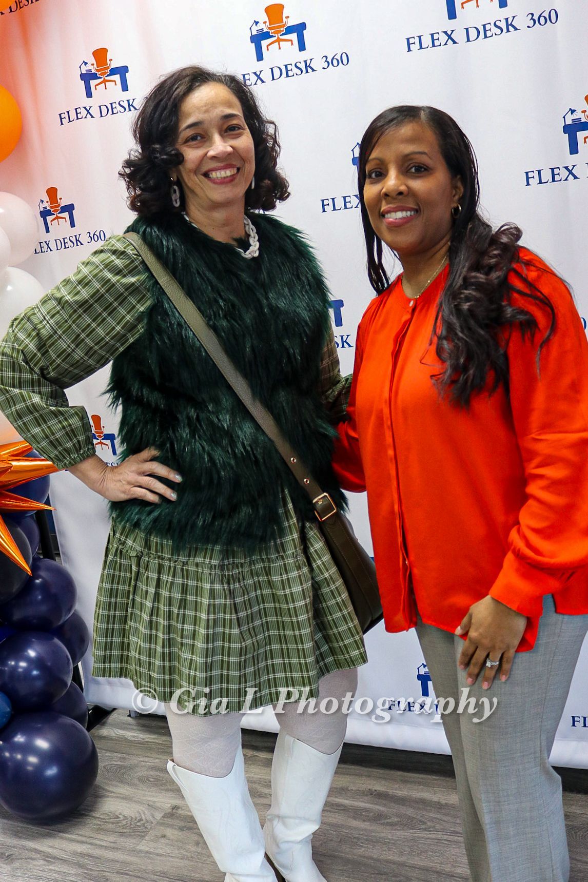 Two women are posing for a picture in front of balloons.