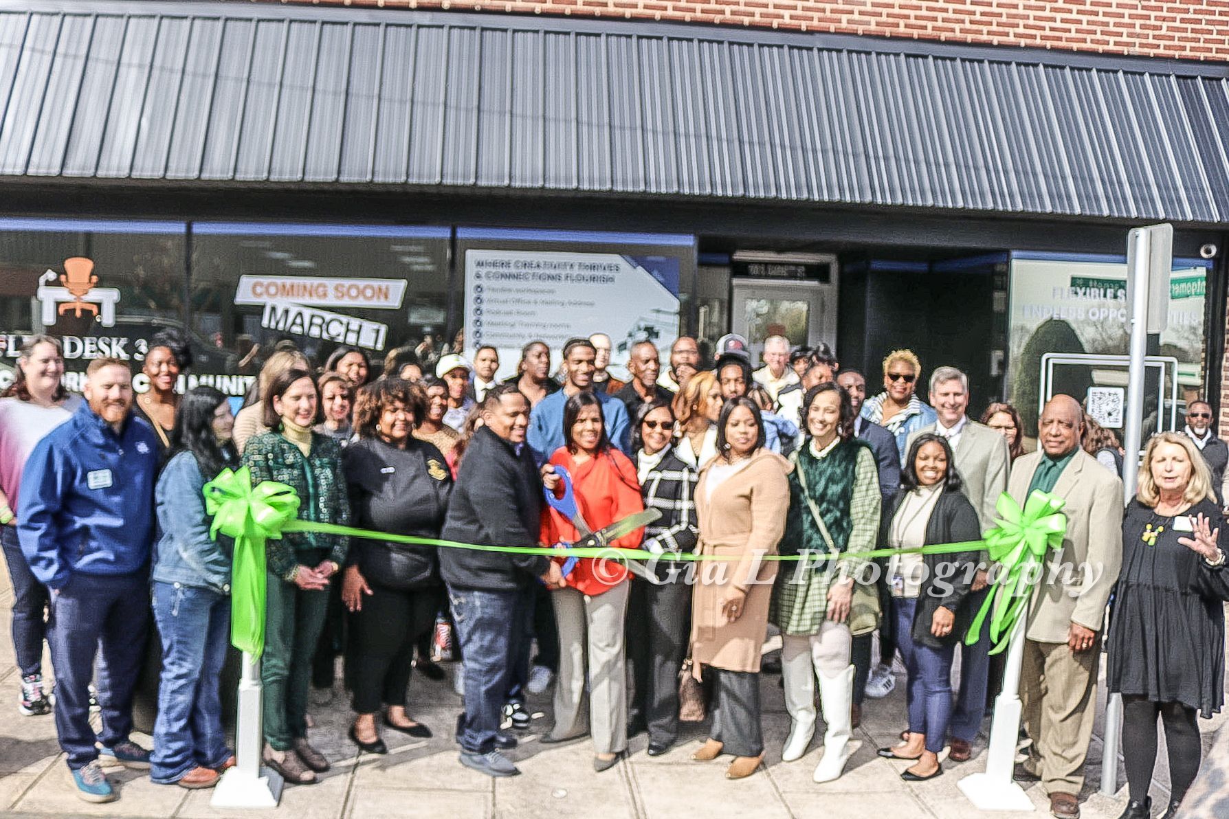 A group of people are standing in front of a building cutting a green ribbon.