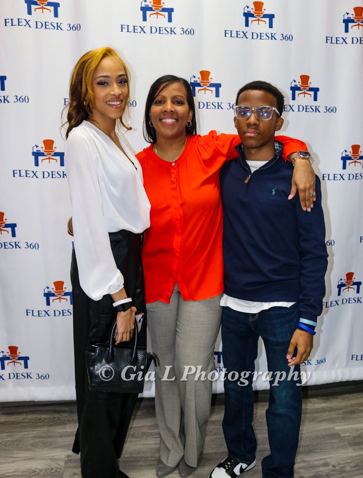Three people posing for a picture in front of a flex desk 360 backdrop