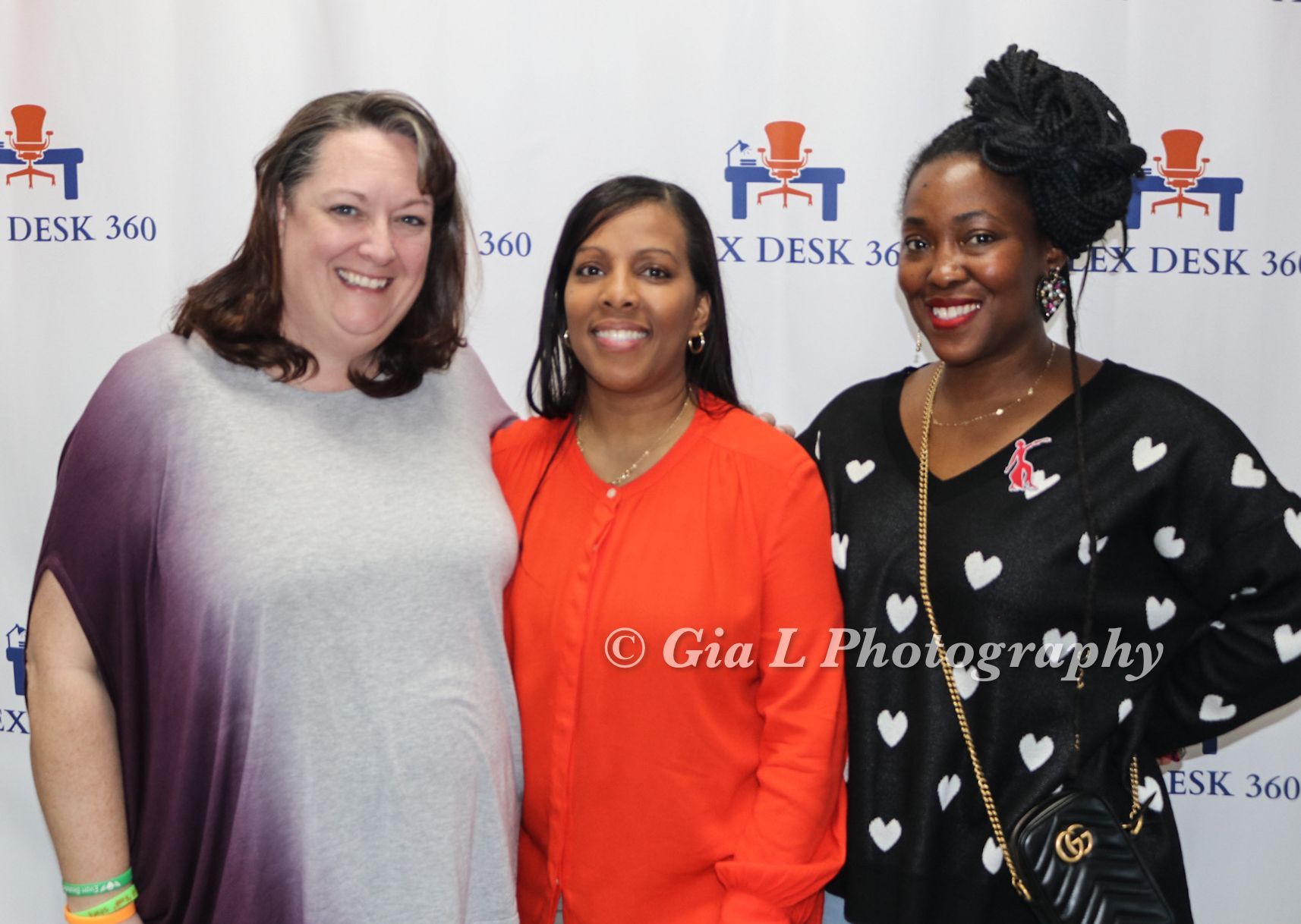 Three women are posing for a picture in front of a sign that says desk 360