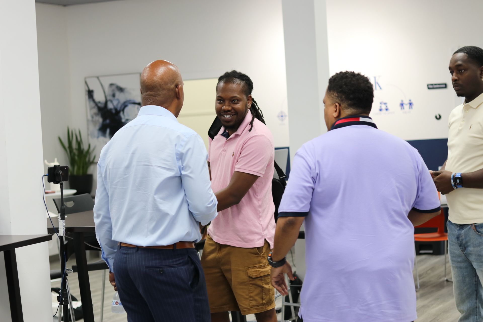 A group of men are standing in a room talking to each other.