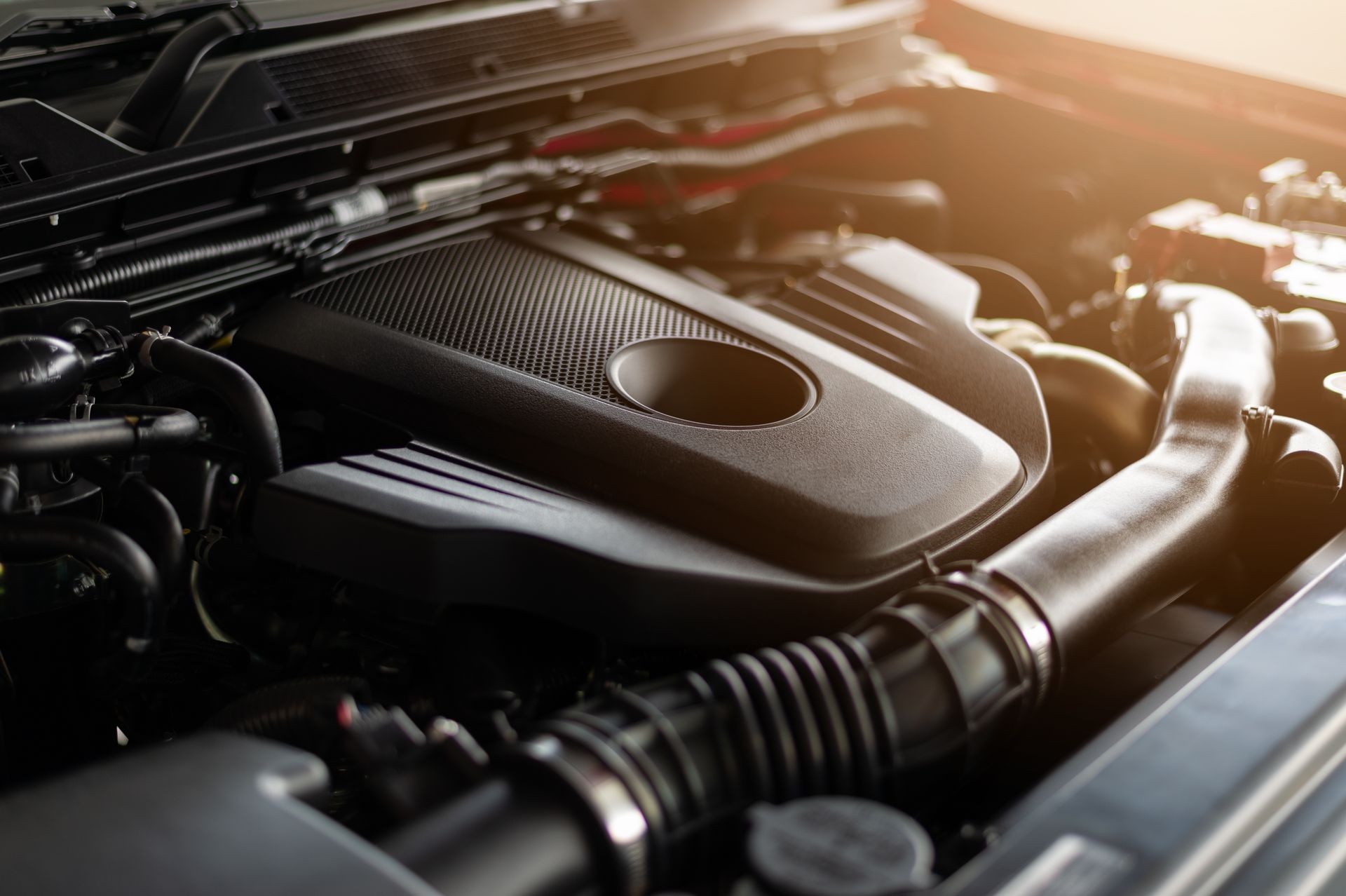 Close-up of a car engine bay with a black engine cover and warm sunlight | Randy Keach Auto Repair