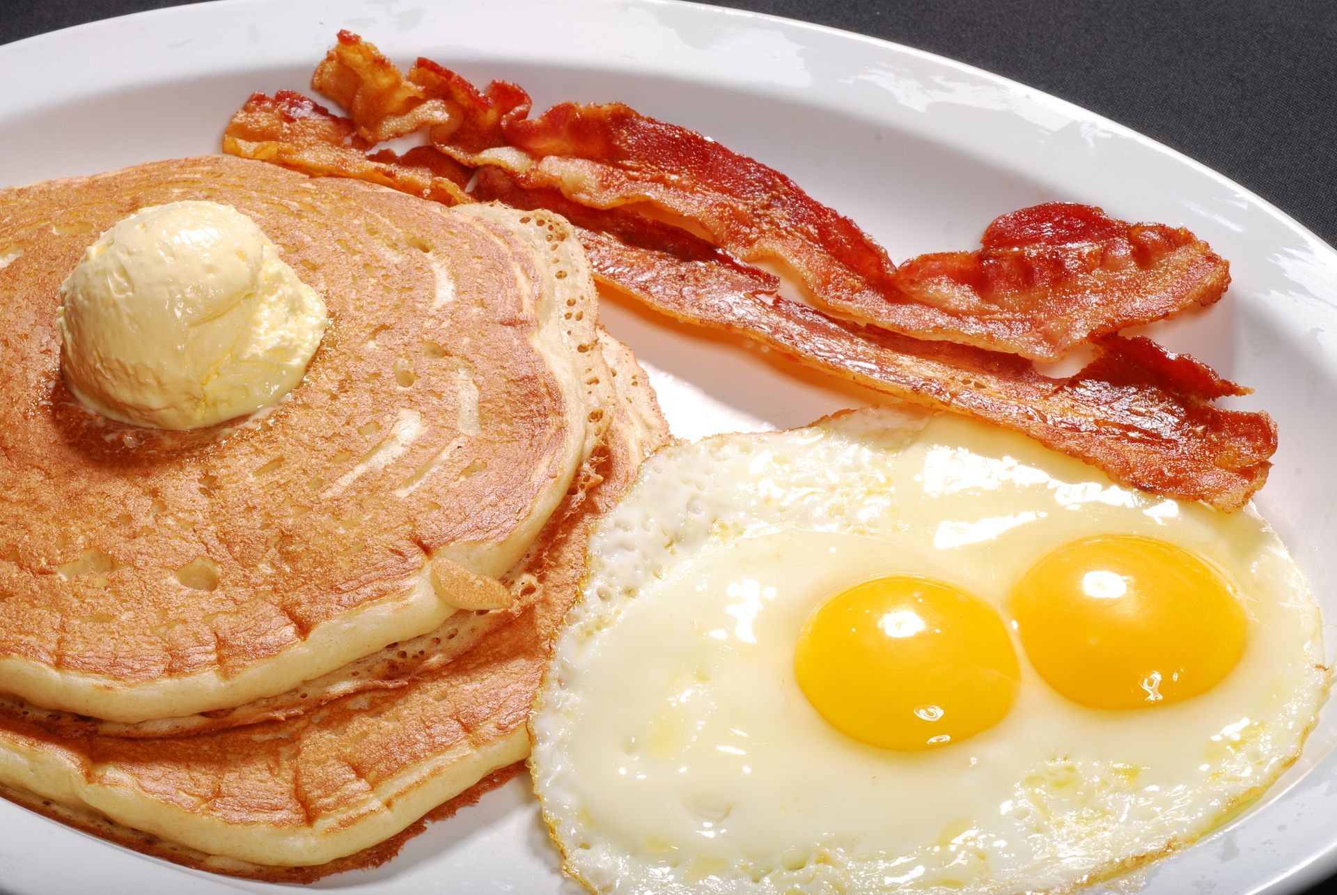 A white plate topped with pancakes eggs and bacon