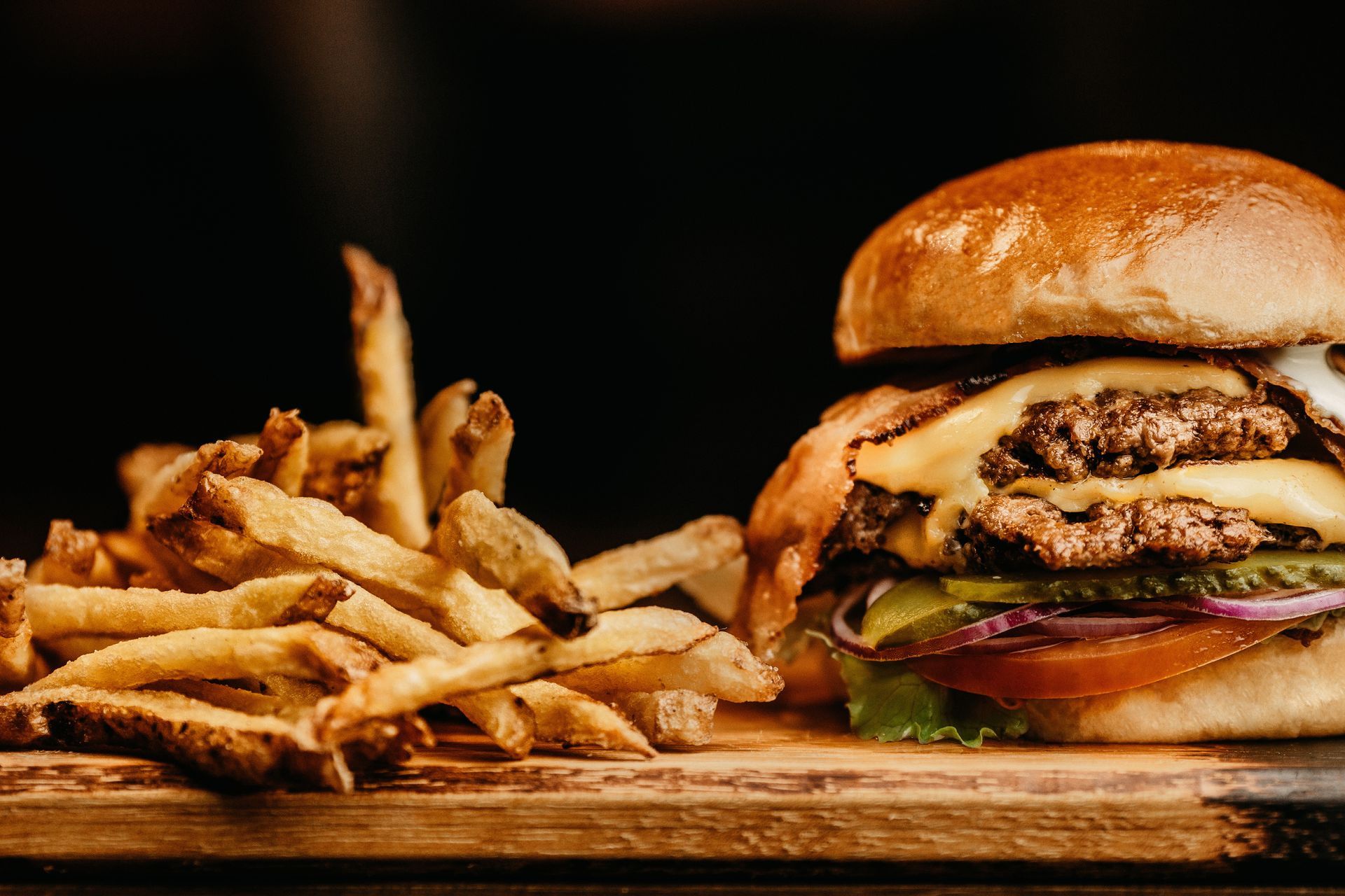 A hamburger and french fries are on a wooden cutting board.divider