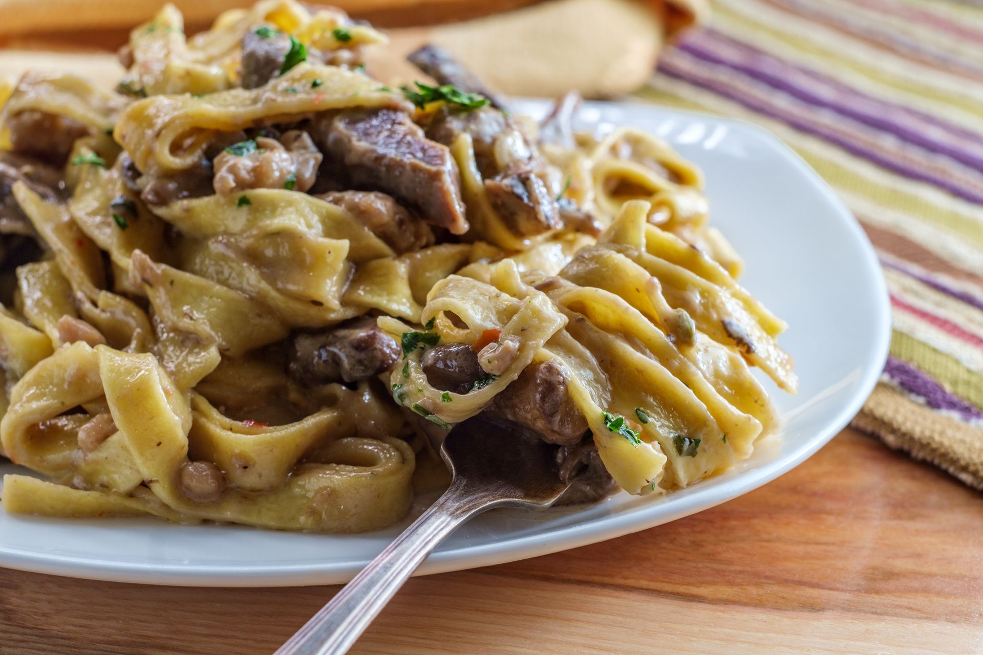 A white plate topped with noodles and meat with a fork on a wooden table.