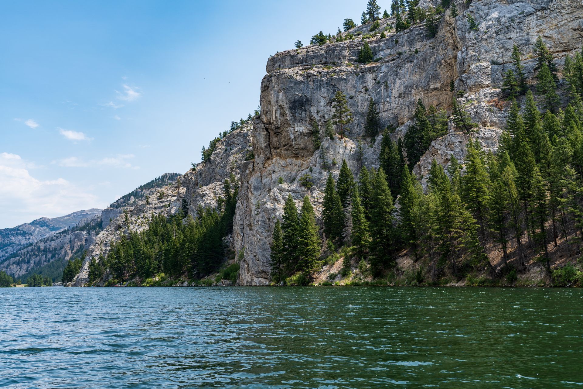 A lake surrounded by mountains and trees with a cliff in the background.