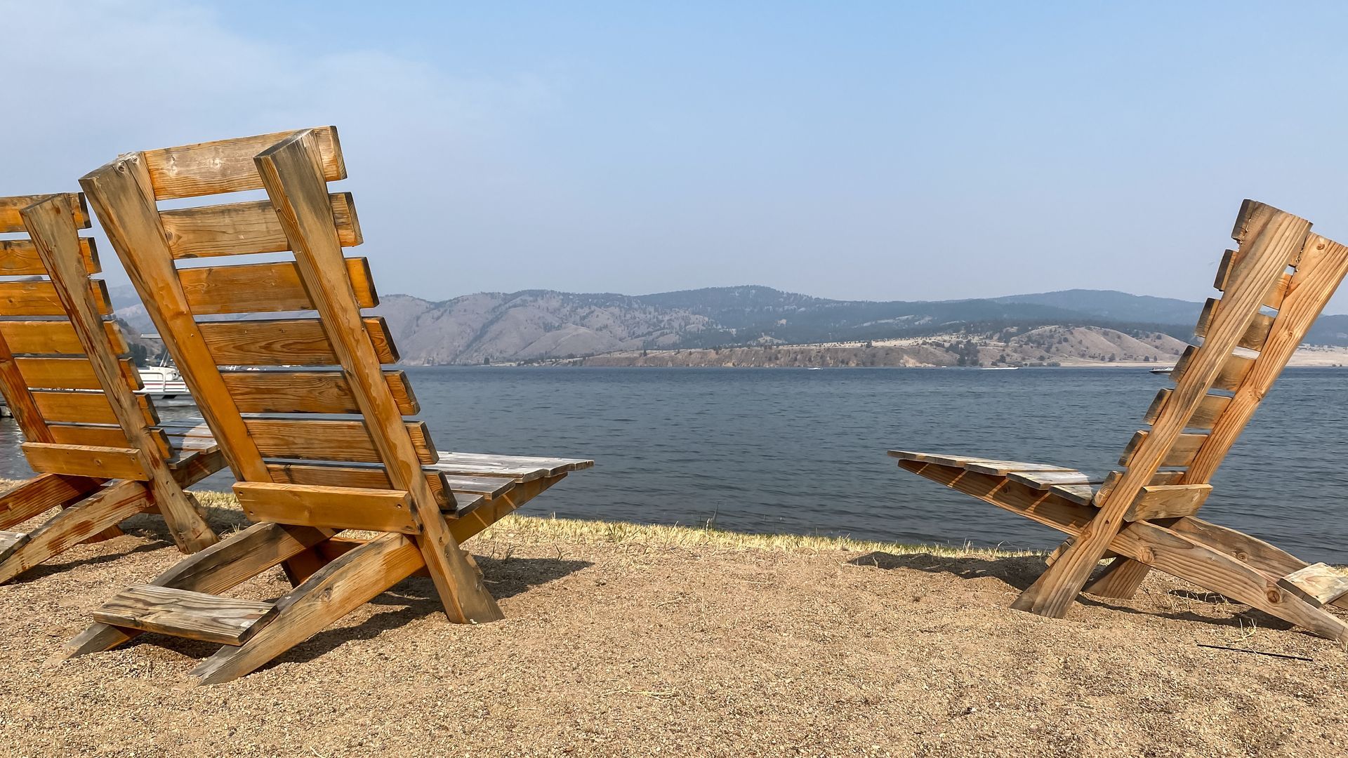 Two wooden chairs are sitting on a beach next to a body of water.