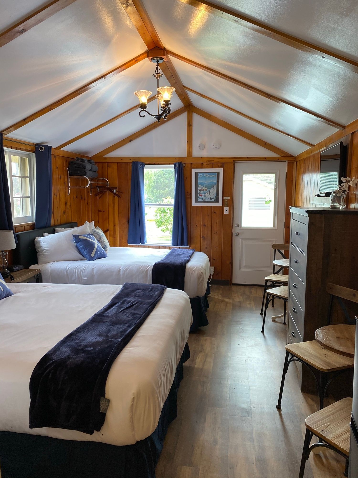 A room with two beds , a dresser , chairs and a window.