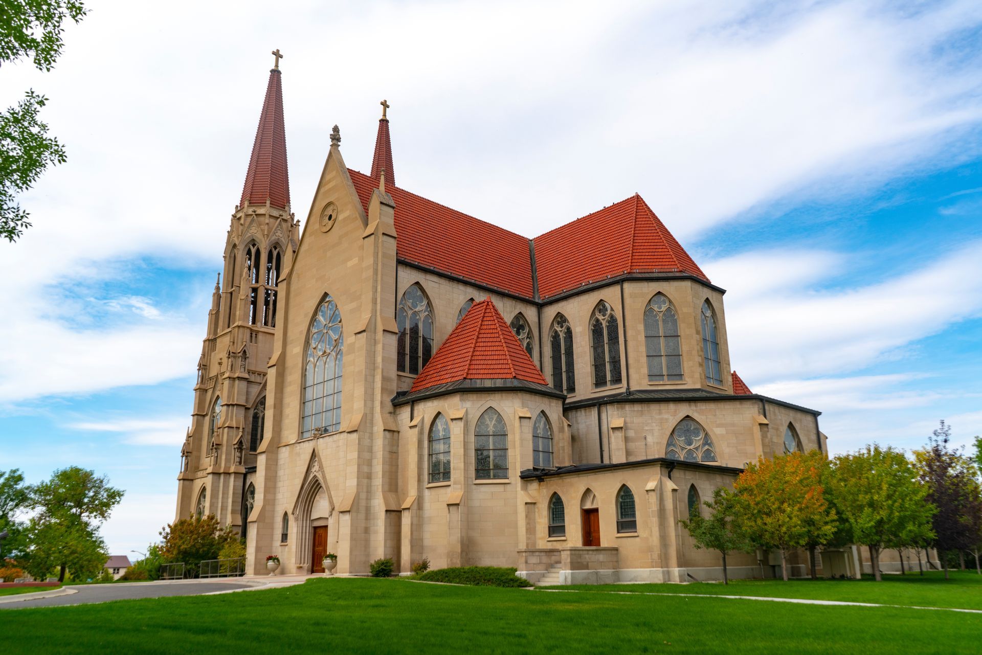 A large church with a red roof is surrounded by grass and trees.