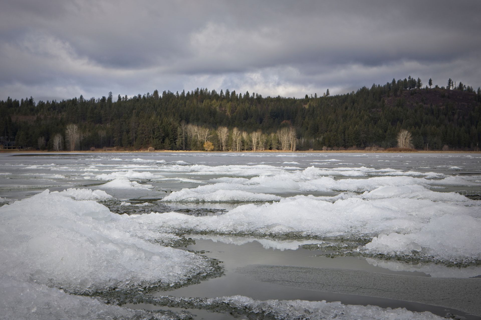 A lake covered in ice and snow with trees in the background