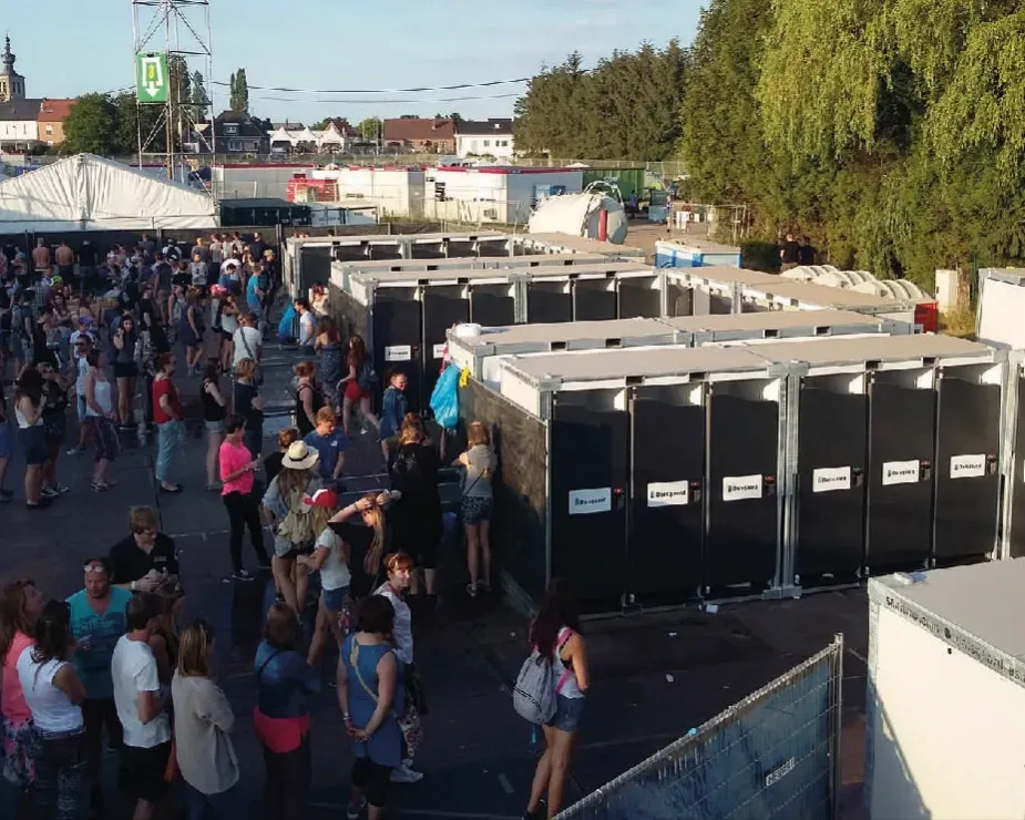 A group of people are standing in front of a row of portable toilets aeroflush at a festival