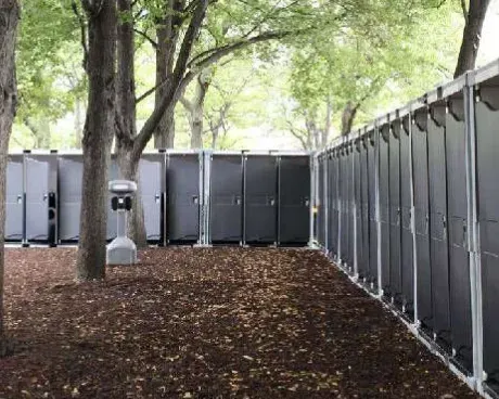 A row of portable toilets in a park surrounded by trees.