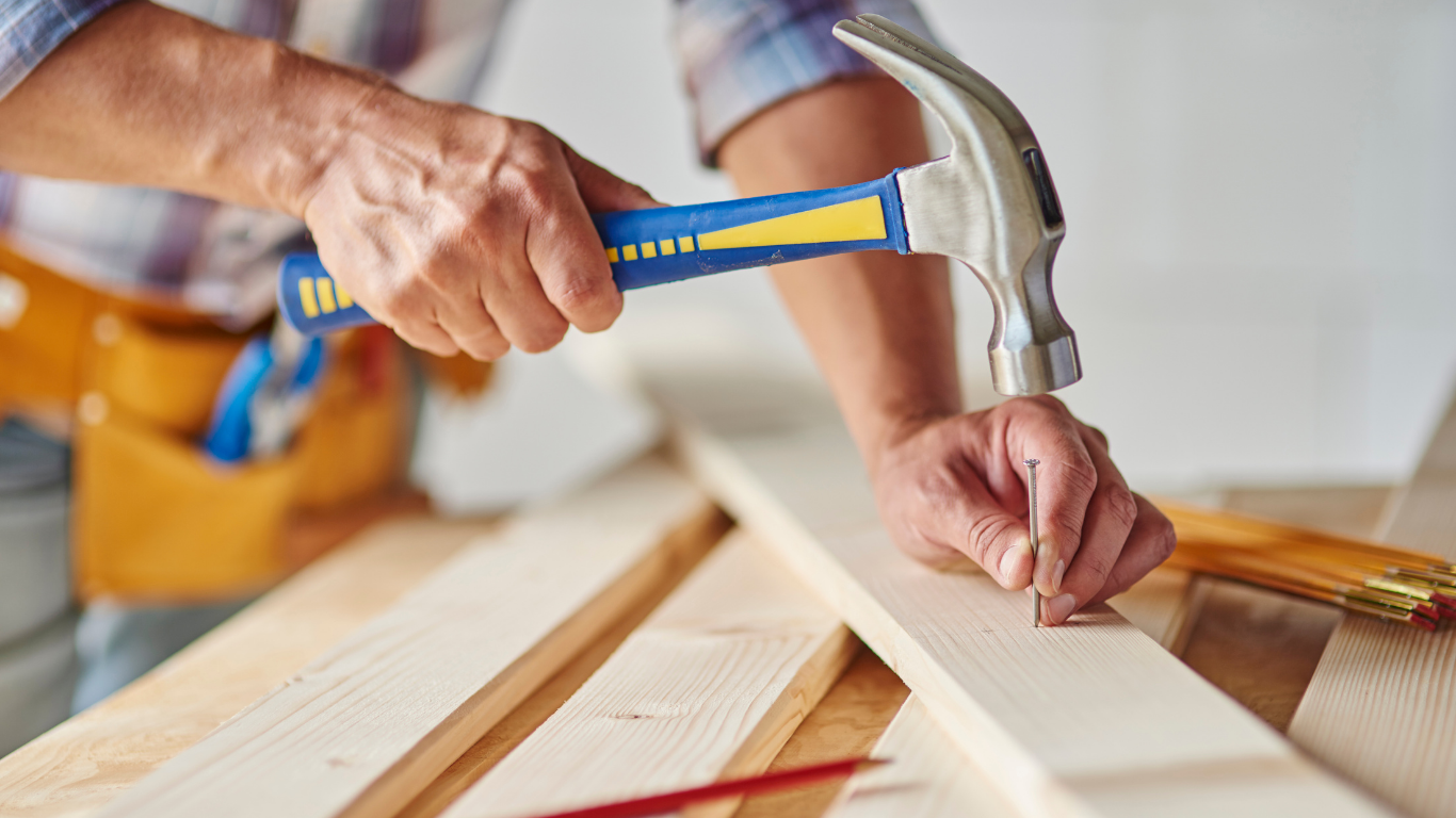 Person hammering a nail into a wooden board.