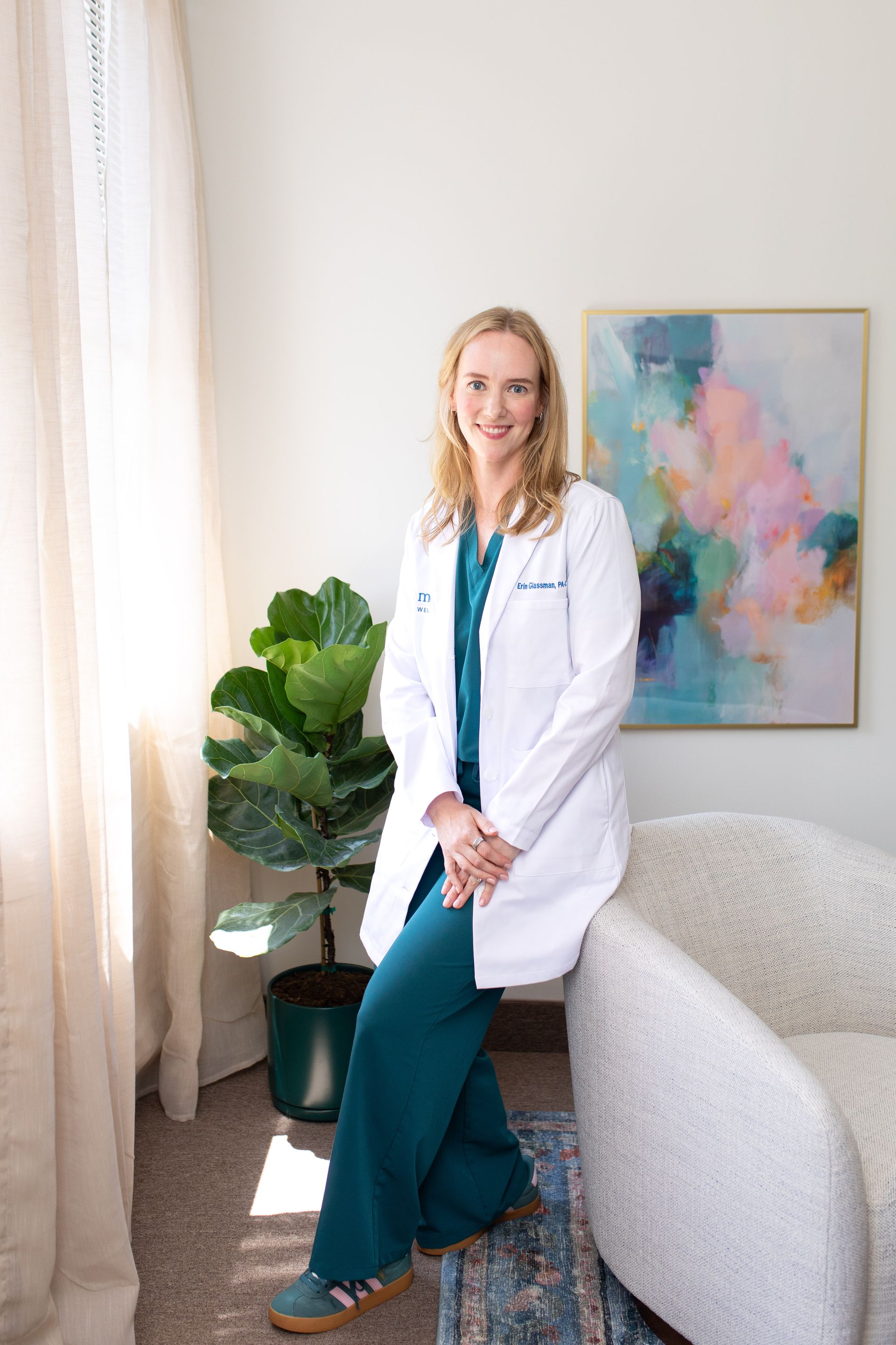 Medical professional in white coat holding a clipboard and vial, smiling in a bright clinic