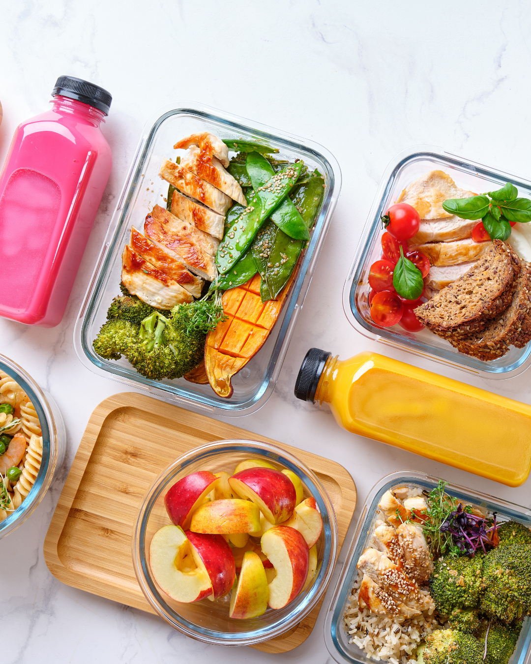 Meal prep containers with grilled chicken, vegetables, fruit, and colorful drink bottles on a white table