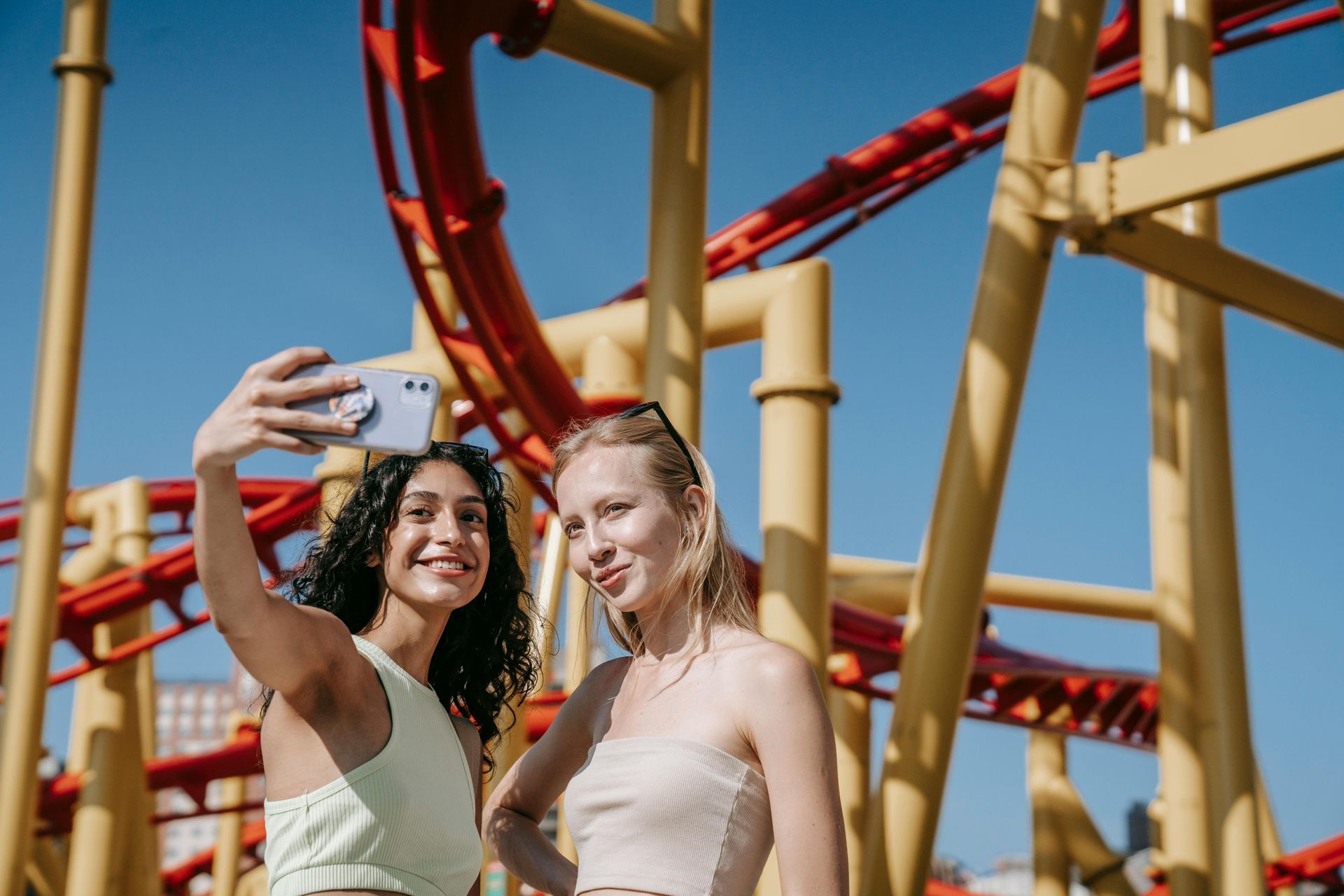Zwei Freundinnen machen ein Selfie vor einer Achterbahn
