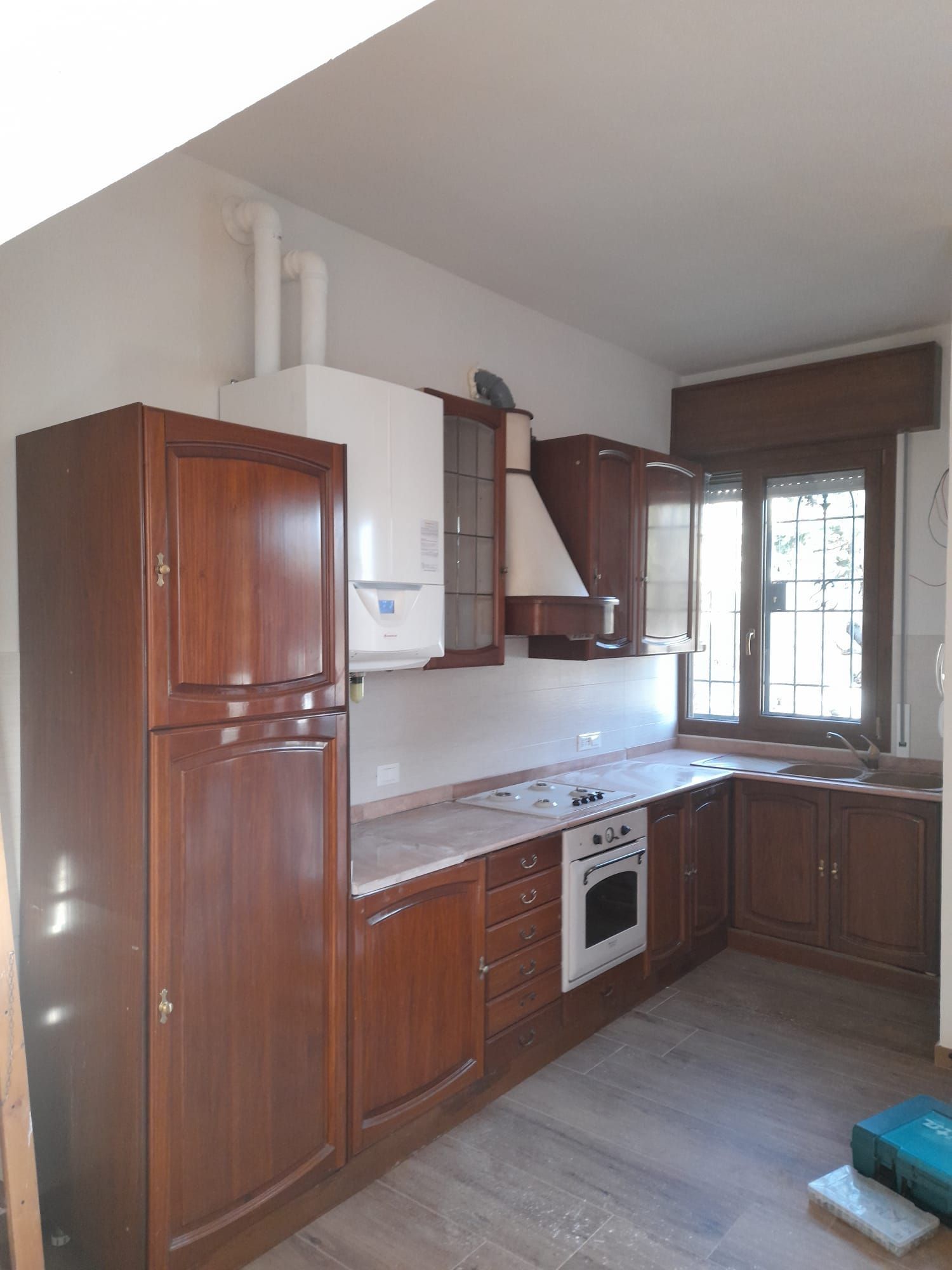 Una cucina con mobili in legno, un frigorifero, una stufa e una finestra.