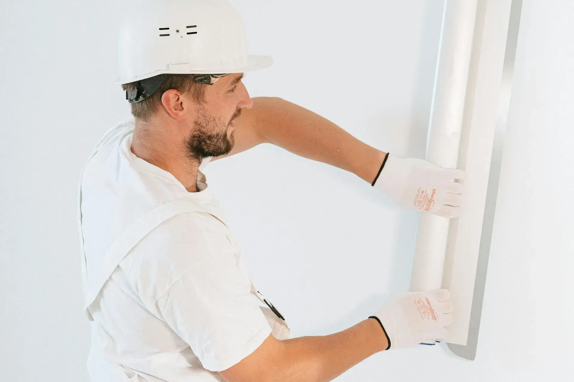 Worker in a white hard hat installing a white wall panel indoors