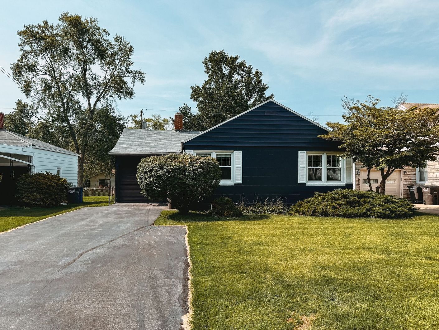 A black house with white shutters and a driveway in front of it.