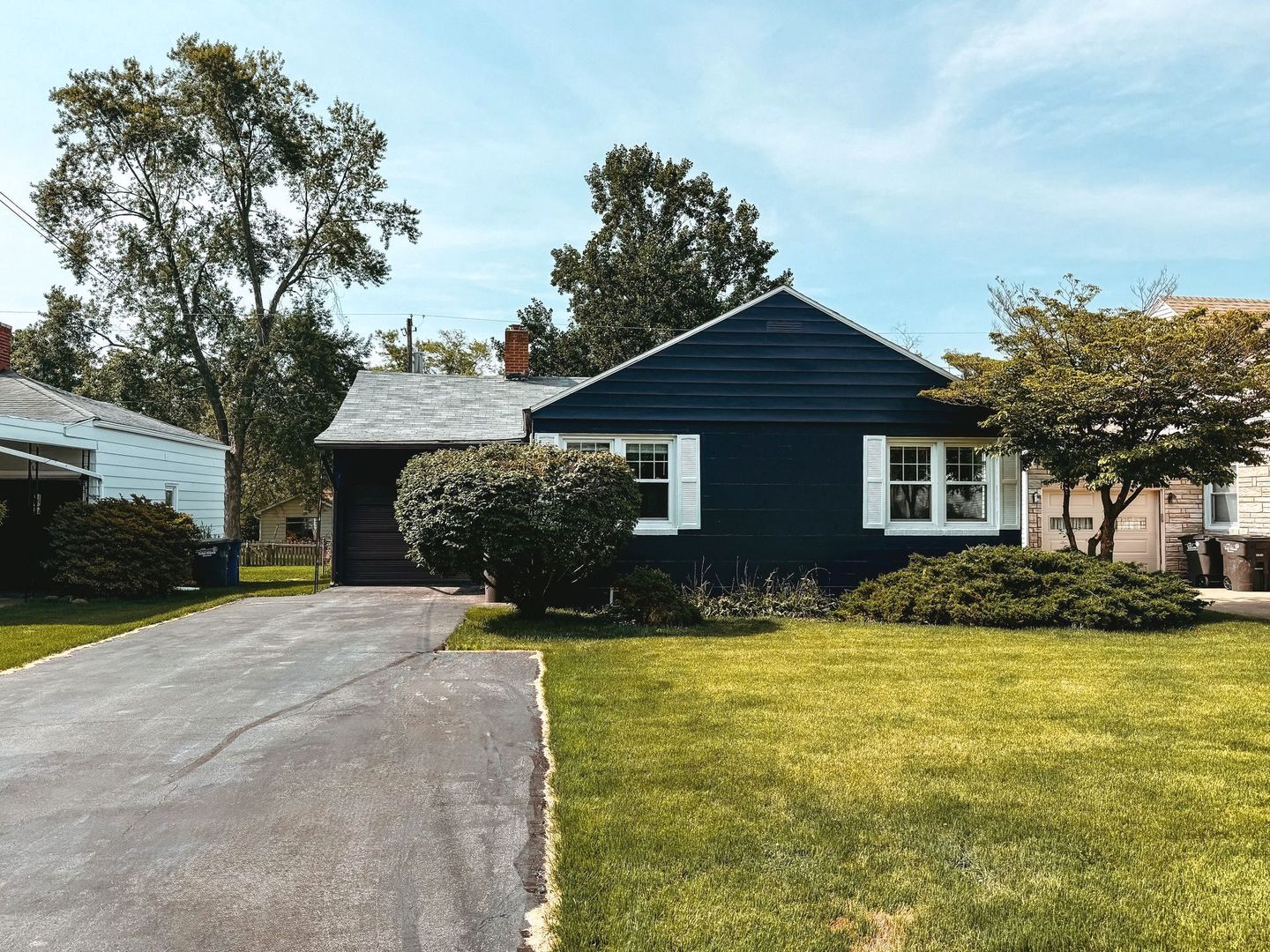 A blue house with white shutters and a driveway in front of it.