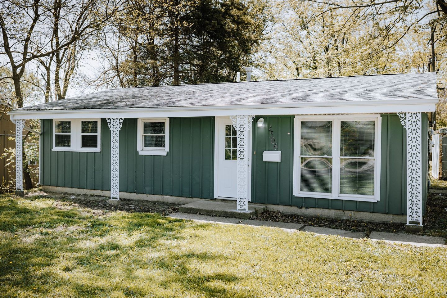 A small green house with a white porch is sitting on top of a lush green field.